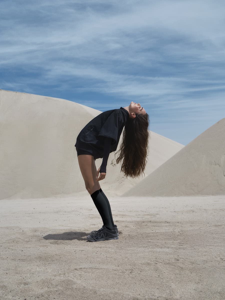 Kirsty Godso wearing black woven layers against the dunes and blue sky
